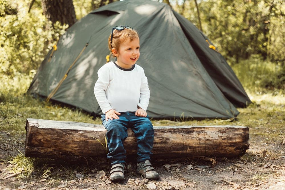 A child sitting on tree trunk with a tent behind