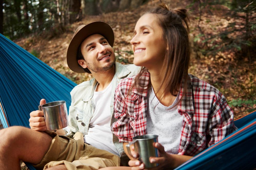 A couple sitting on a hammock in the woods