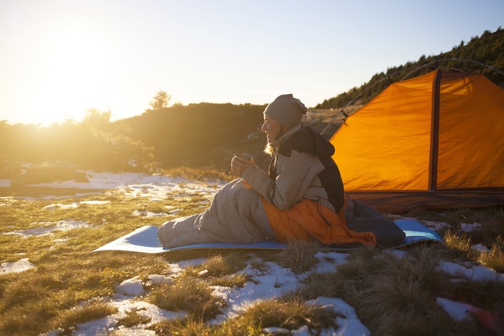 Woman sitting and drinking beside the camping tent