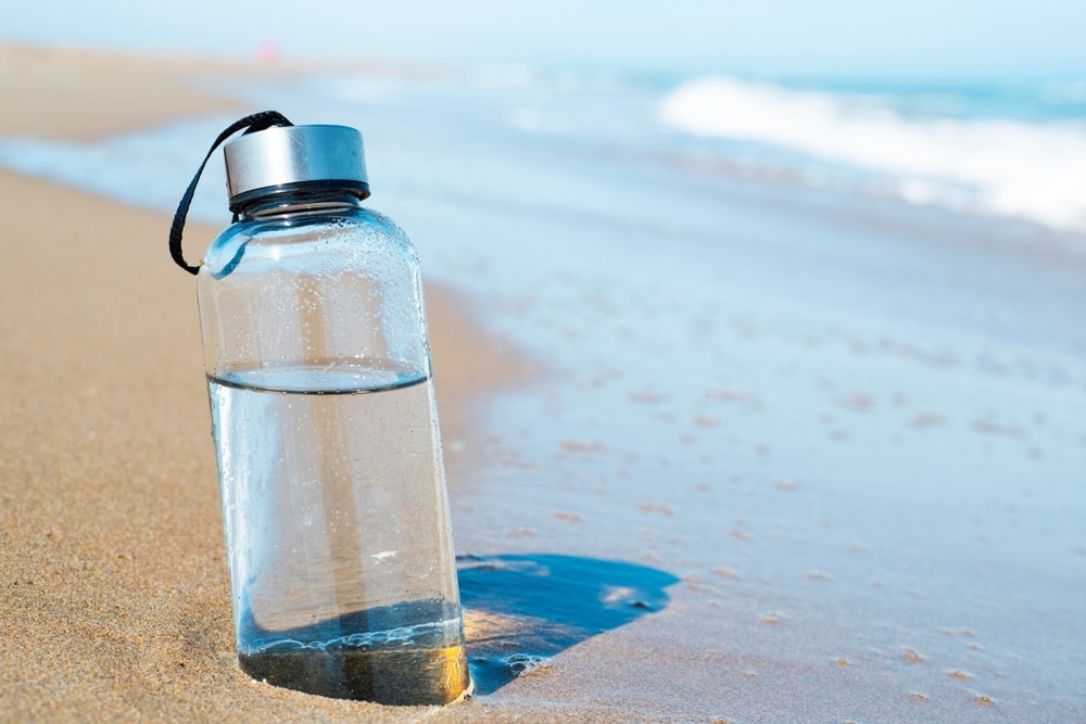Water bottle with half part buried on the beach sand