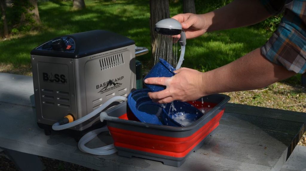 Man washing plates using a water heater while camping