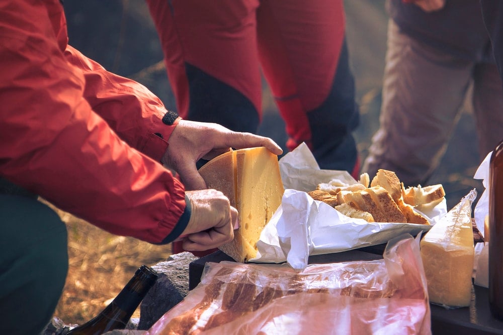 Group of campers slicing a cheese as their camping food