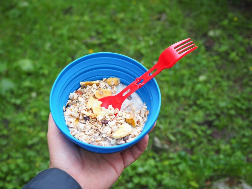 A person holding a bowl with granola as part of her camping snack