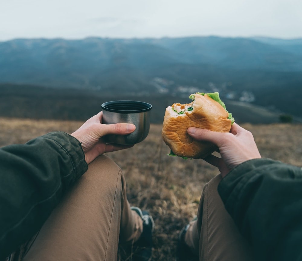 Holding a cup and a burger as camping food