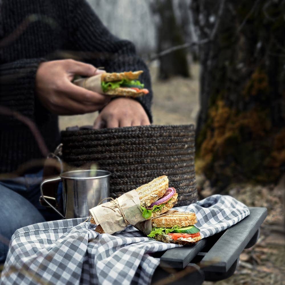 Man holding sandwich and others displayed on the table as camping food