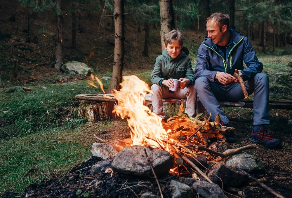 Father holding camping firewood while talking to son