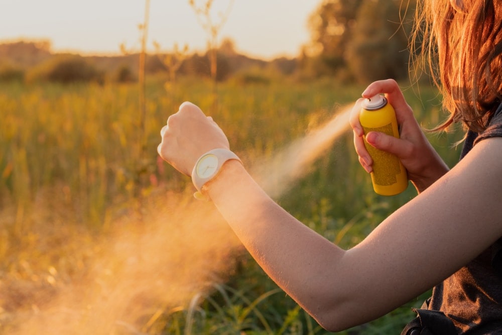 Woman spraying bug spray to her skin while camping