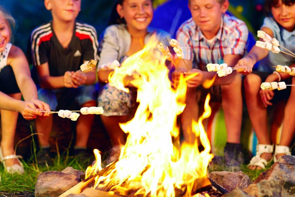 Children holding marshmallows over a campfire and playing a camping game
