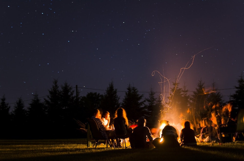 Group of people chilling under a night sky and doing a campfire games