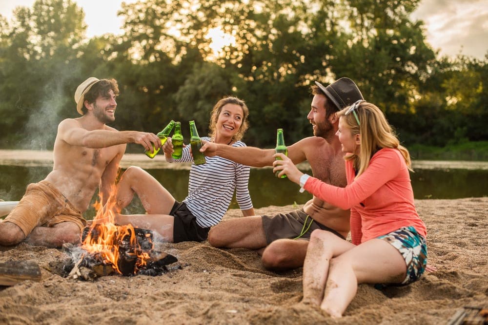 Four friends drinking and playing camping games around a campfire