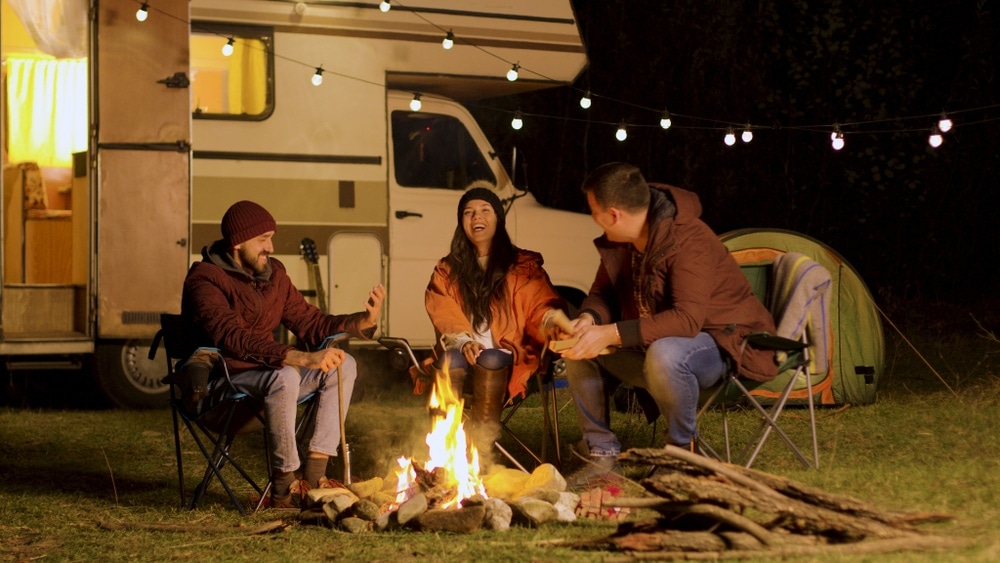 Three friends sitting on a camping chair talking and playing campfire games