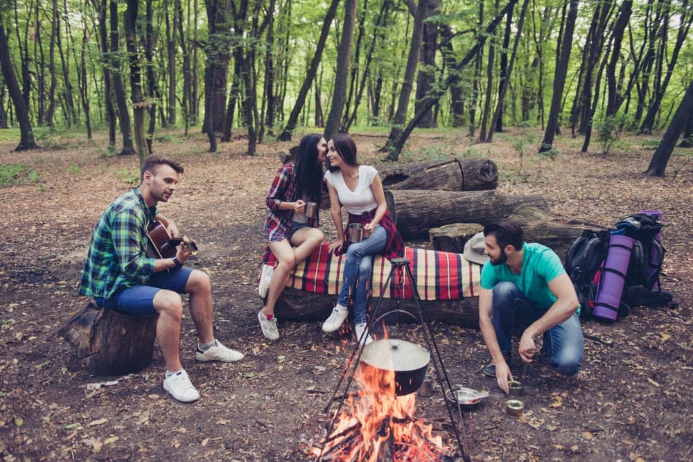 Four friends cooking, talking and playing campfire games