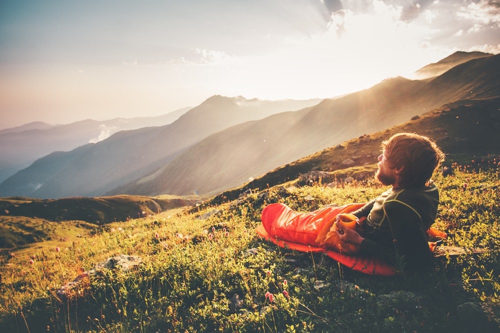 Man with sleeping bag liner watching sunrise at the top of the mountain