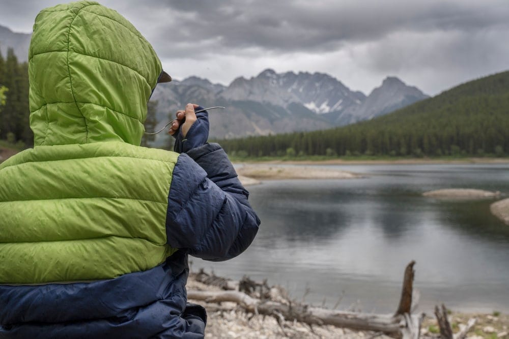Person's back wearing a jacket looking at a lake
