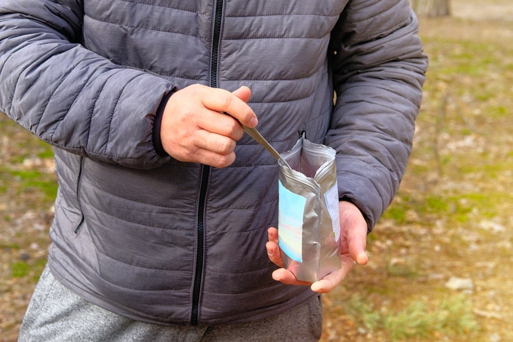 Man holding a spoon and a odor-free storage bag while camping