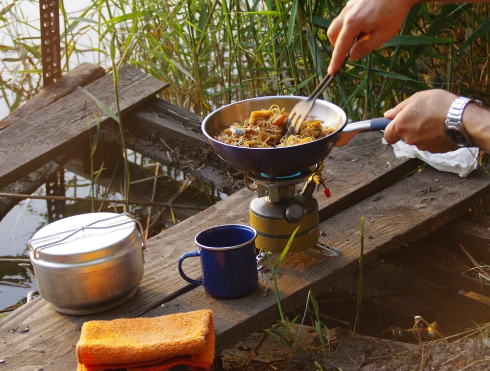 Backpacker cooking using a camp stove on the shore of the lake.