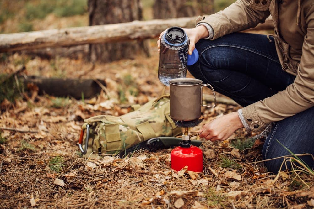 A hiker pouring water on an empty big camping mug 