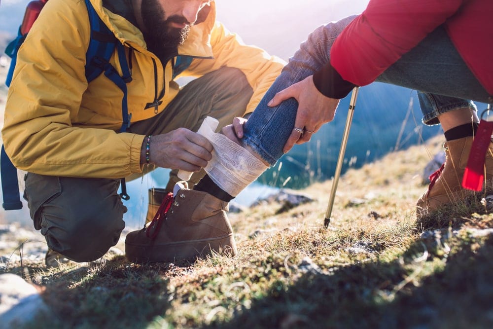 Hiker wrapping a bandage on another hiker's ankle