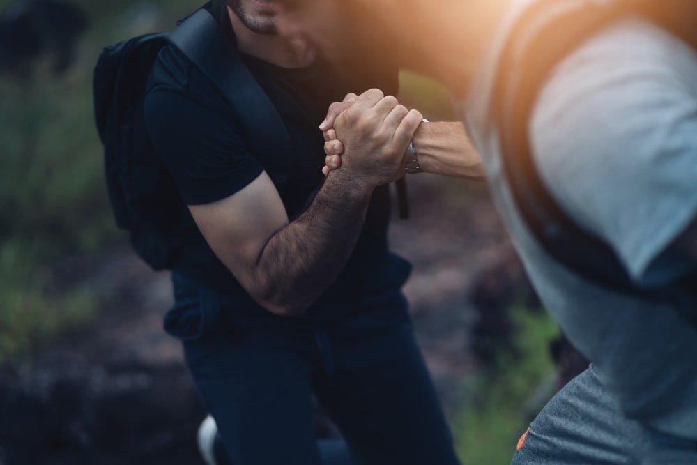 One hiker helping a hiking buddy on a trail
