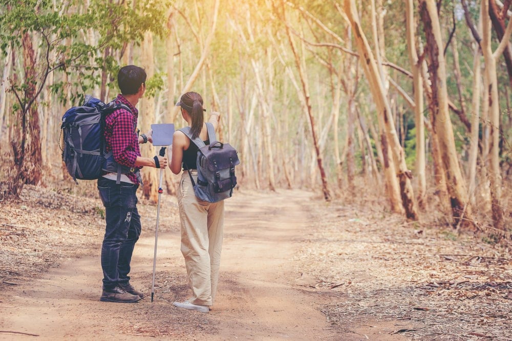 Couple hikers looking at their big gps navigator with the girl pointing direction in the forest