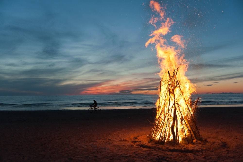 Big bonfire on a beach with man bicycling in the background