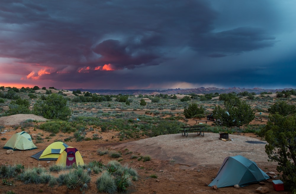 Three small camp tents in a desert with thunderstorm and dark clouds