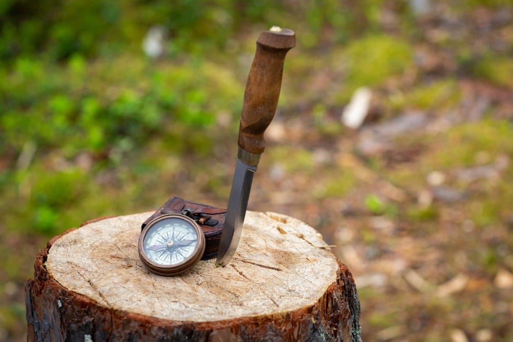 A hiking knife and a compass on a tree stump