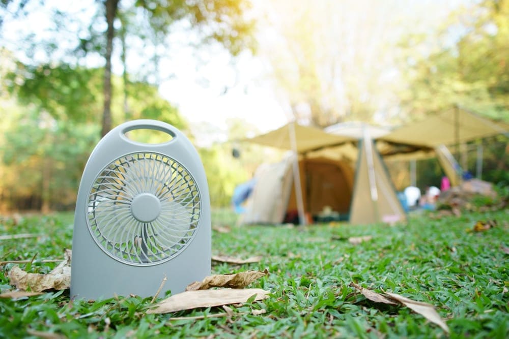 Mini fan on a grass with a blurred camping tent in the background