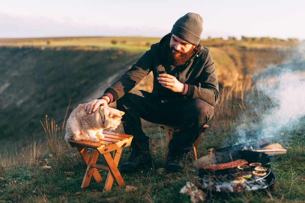 A man near a campfire touching the cat