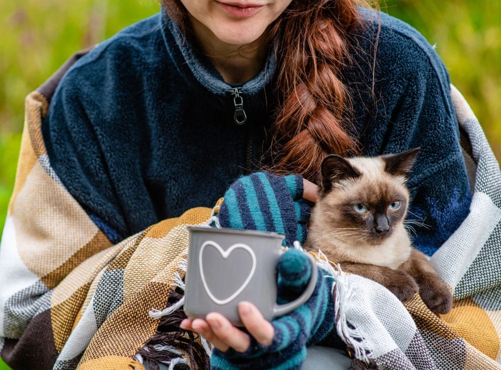 Woman carrying her cat while holding an enamel cup