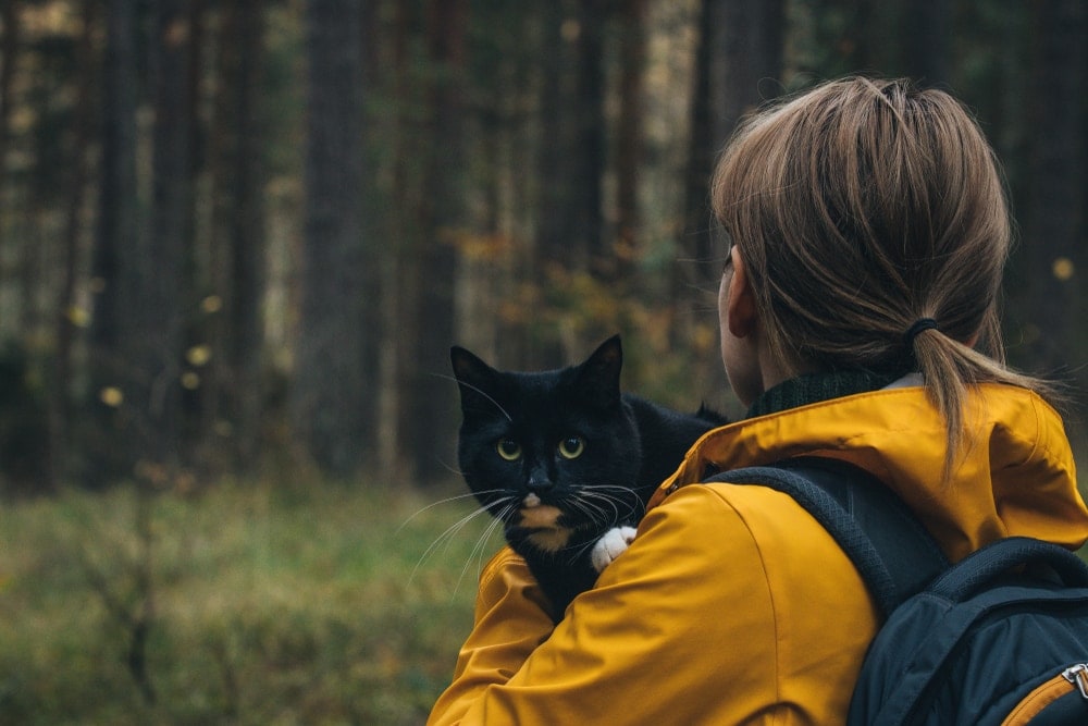 Woman carrying a black cat going into the woods