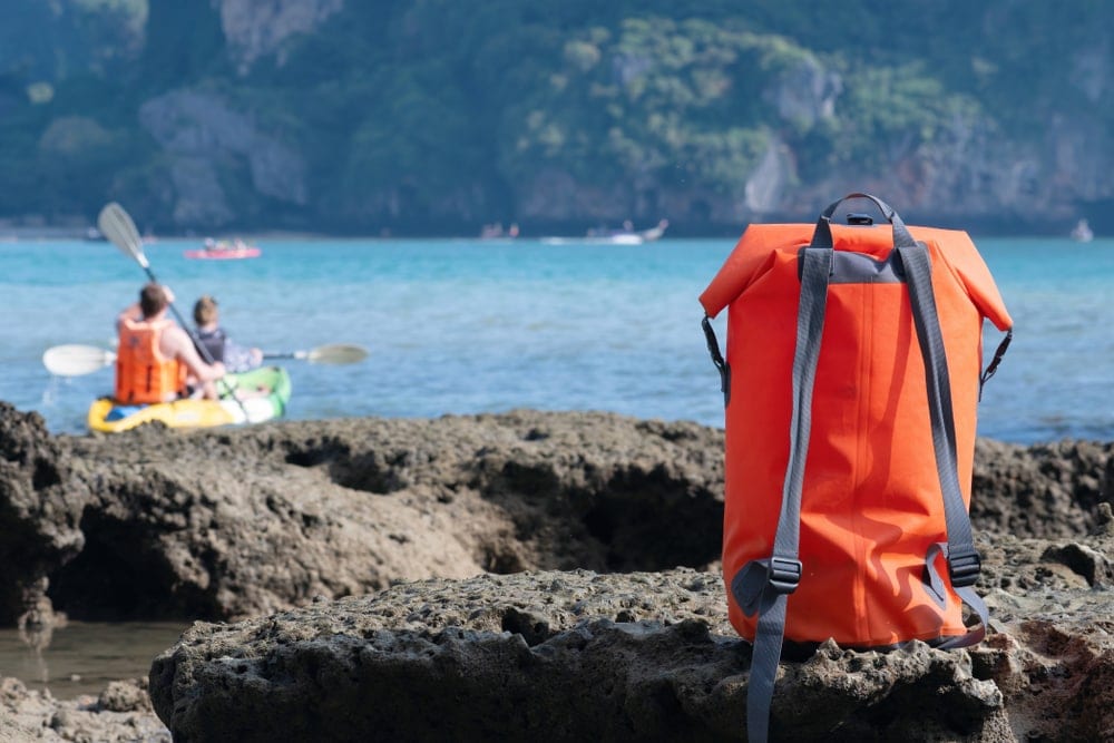 Backpack on a rock with couple rowing a boat
