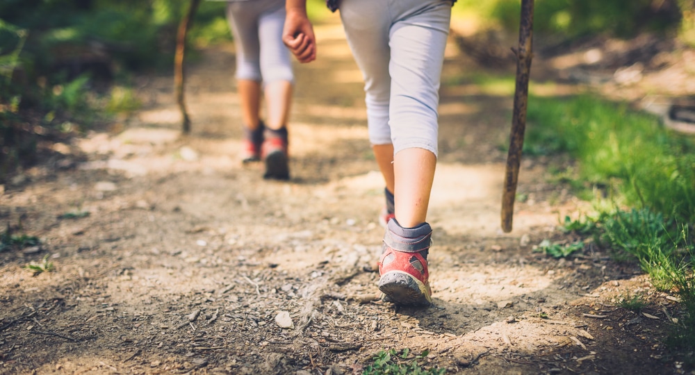 couple walking trough forest path wearing mountain boots and walking sticks.