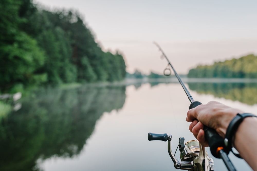Fisherman with rod, spinning reel on the river bank on a sunrise in a lake