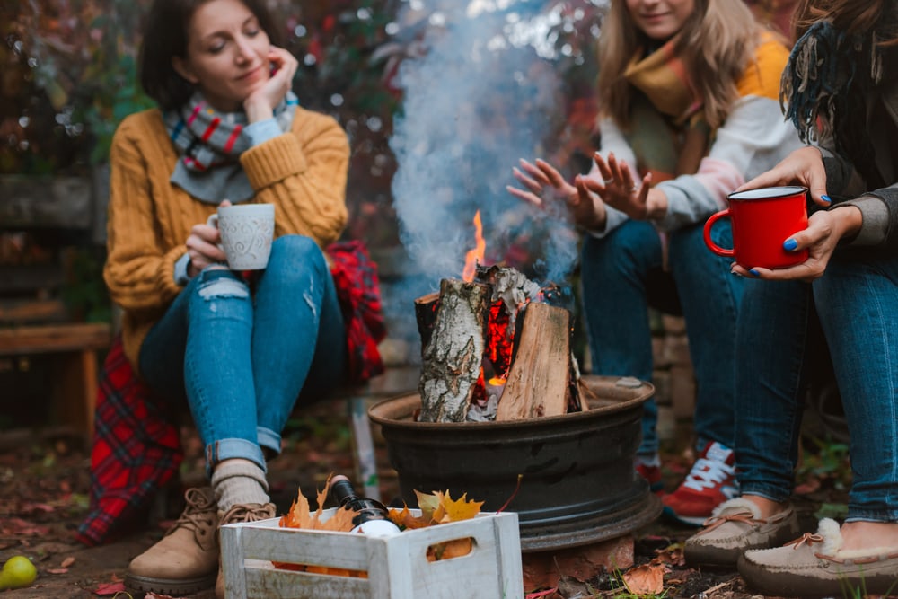 friends relaxing and drinking  while warming themselves by a campfire in the wilderness