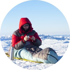 a man sitting up and drinking coffee in his sleeping bag
