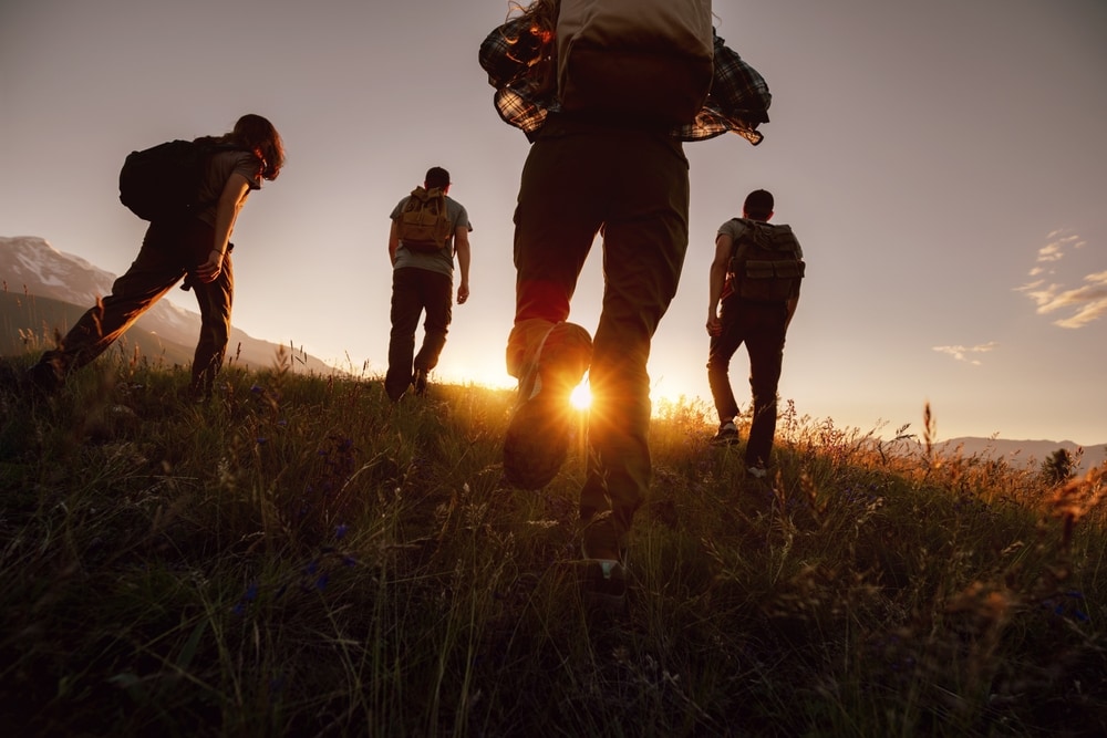 Silhouettes of four young hikers with backpacks at sunset