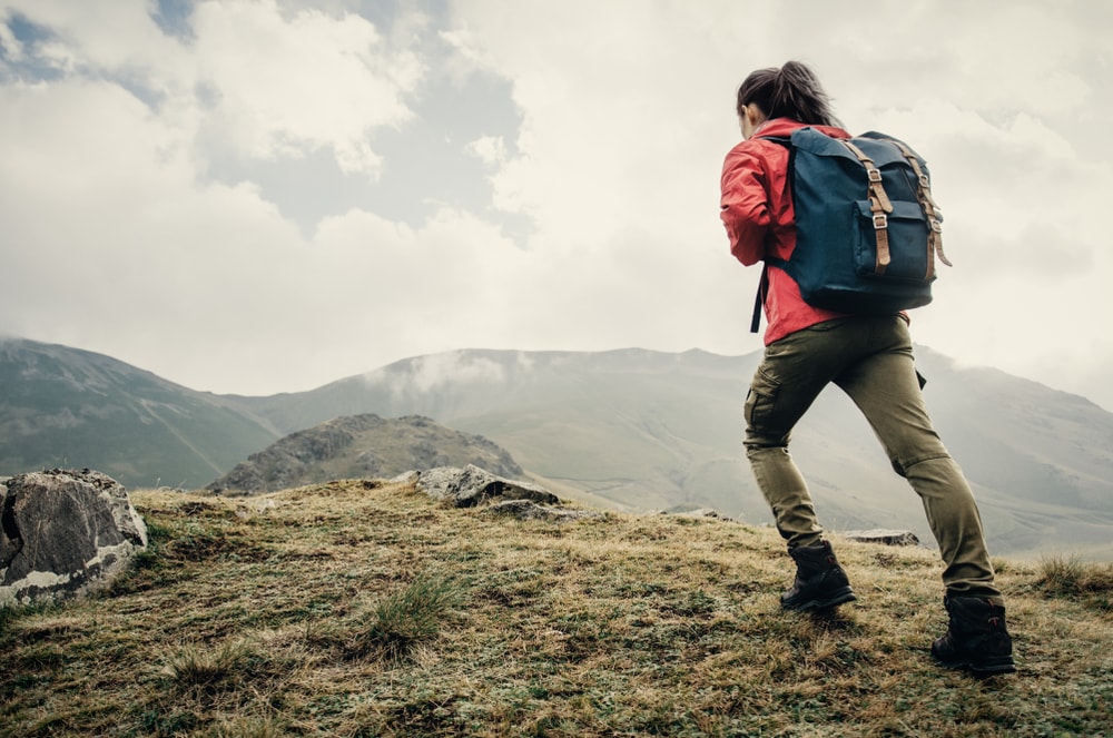 Woman in backpack and hiking pants going up in the mountains