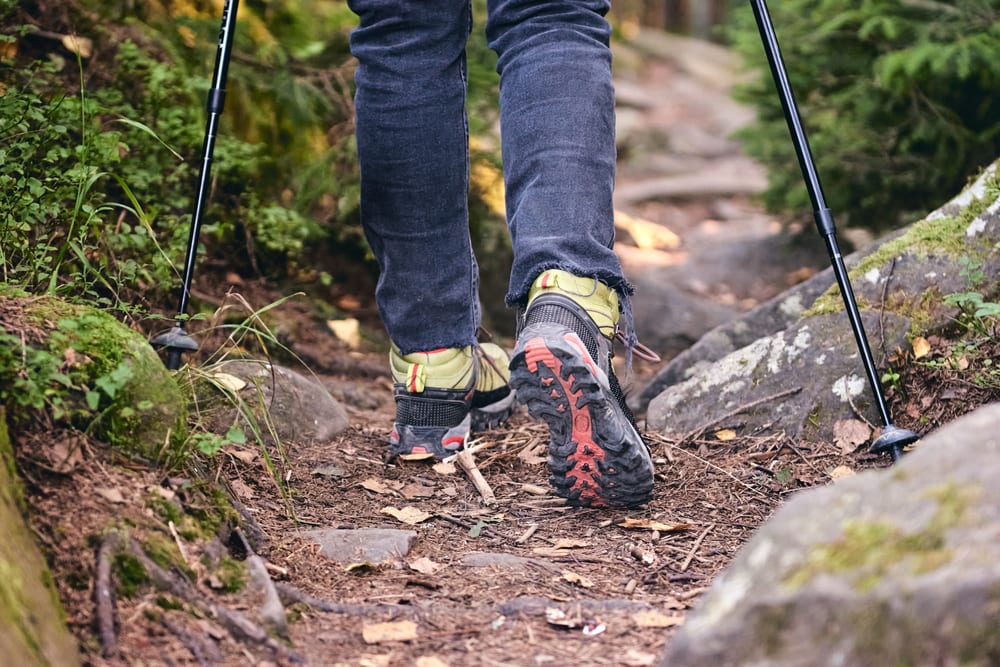 A hiker in jeans using trekking poles 