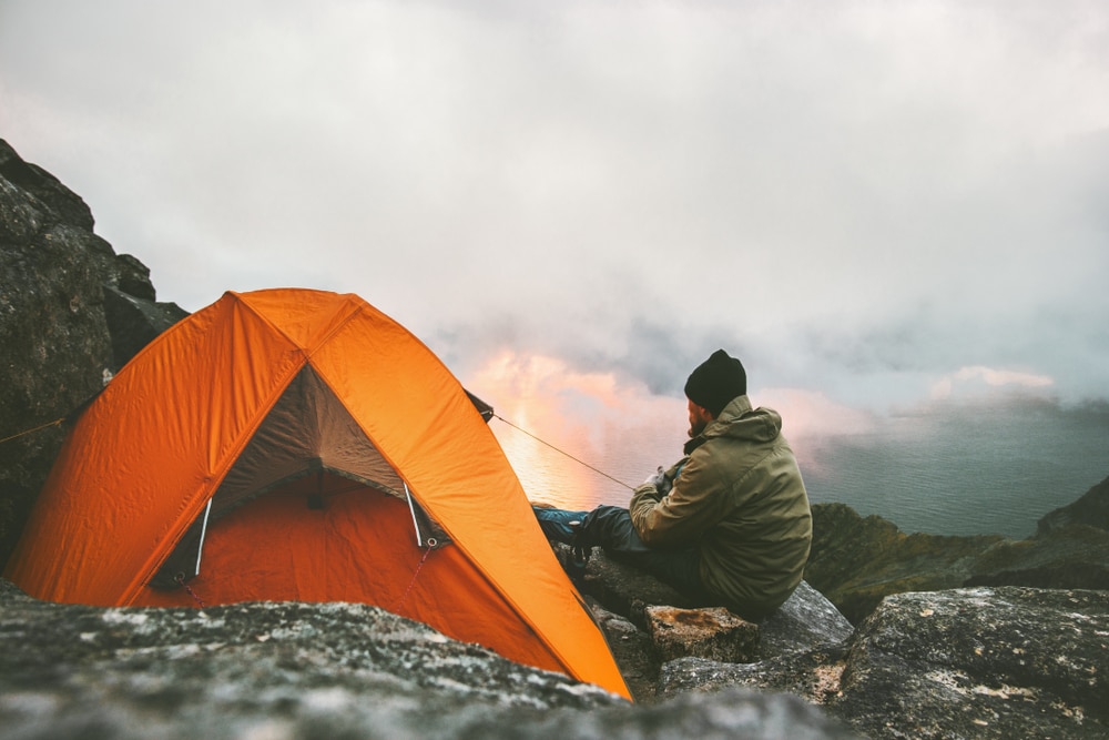 A hiker relaxing by the tent and campfire on the mountains