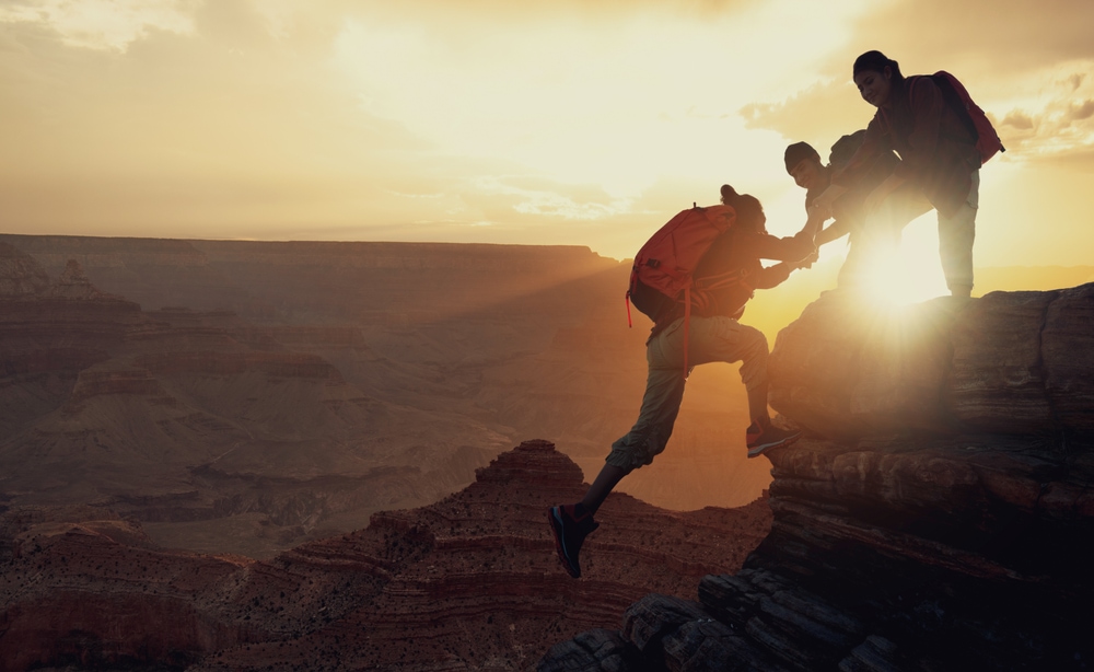 Three hikers climbing up on the peak of mountain.